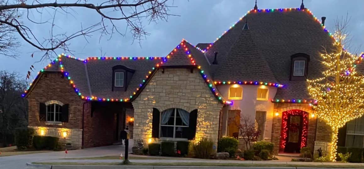 Christmas lights on a stone house at dusk.